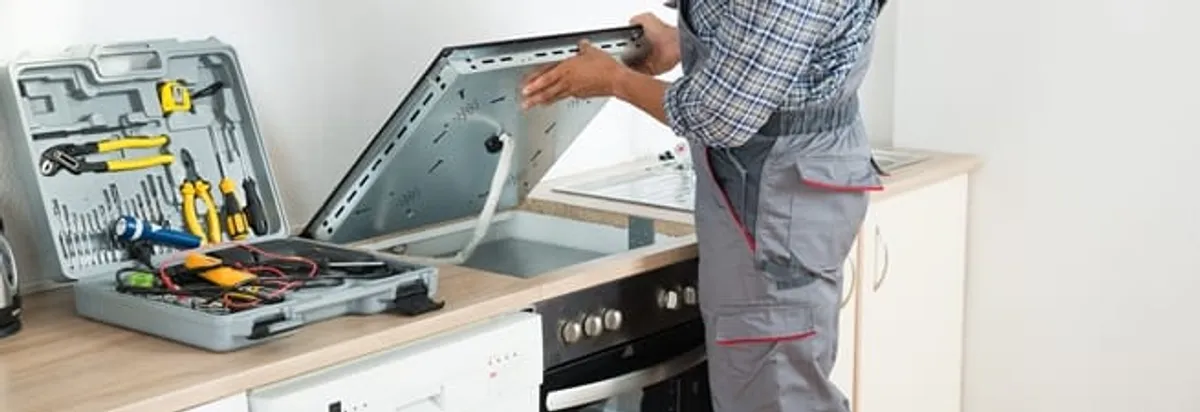 Cooktop repair technician lifting a built-in stovetop for service in Baton Rouge, LA