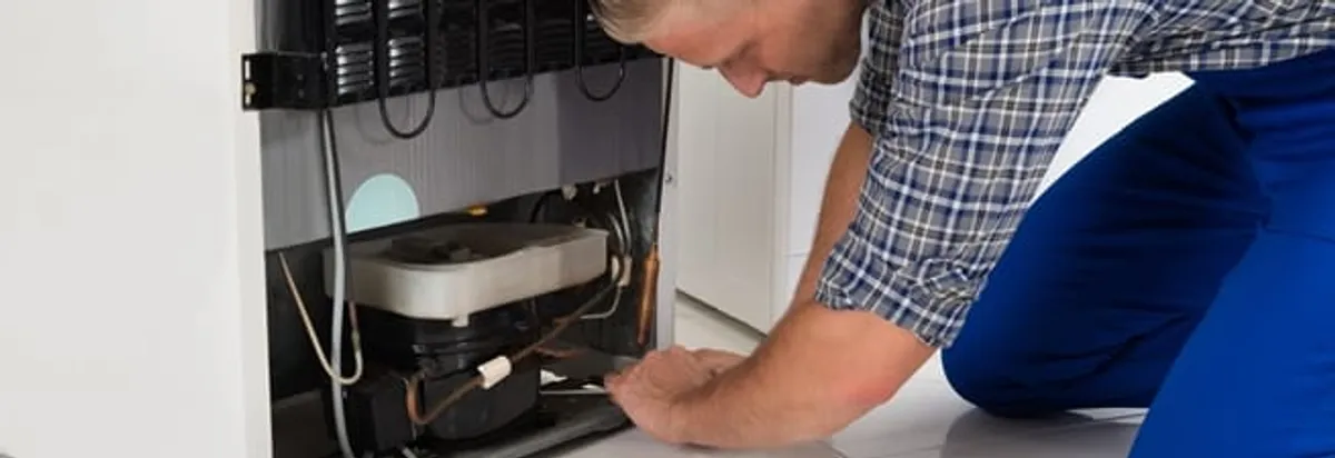 Refrigerator repair technician servicing the compressor and condenser area in Baton Rouge, LA